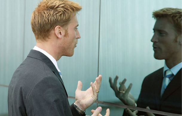 A man looking at his reflection in a two-way mirror.